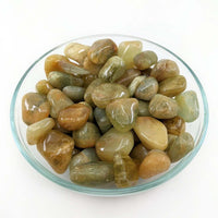 Polished Moonstone pebbles in a glass dish enhancing the beauty of Golden Beryl