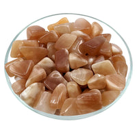 Polished peach moonstone crystals in a glass dish with Honey Calcite Tumbled Stone