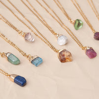 Delicate gold-toned birthstone necklaces with raw gem pendants in green, purple, blue, amber on 16-18 inch adjustable brass chains