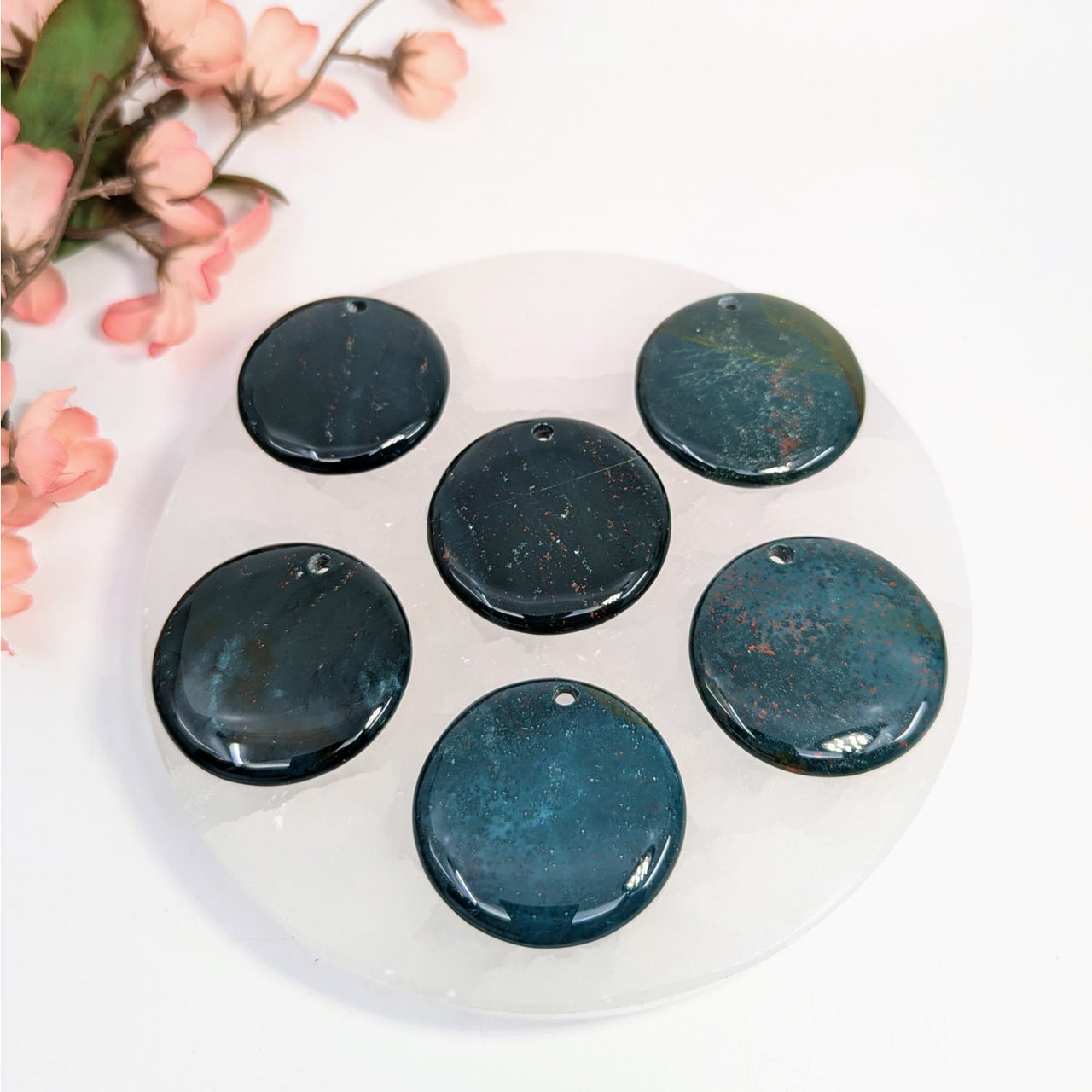 Seven polished bloodstone pendants displayed in a bloodstone 1.5-inch flat round drilled pendant