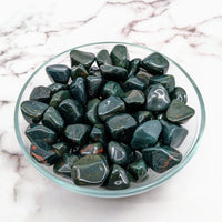 Arafed glass bowl of Bloodstone Green tumbled stones on a marble table