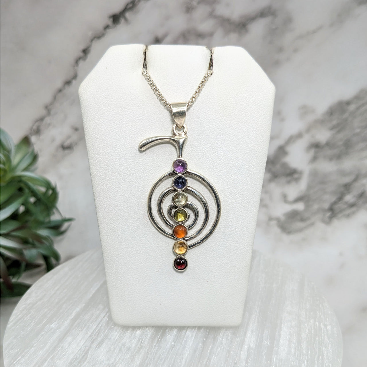 Cho Ku Rei 1.7’ Chakra S.S. Pendant #LV5133 with three colored stones on a white stand