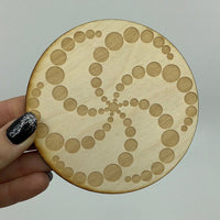 A person holding an alder wood Crop Circle Crystal Grid wooden coaster with intricate circles