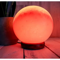 Globe Shape Salt Lamp glowing on a wooden table, available in 5’ and 7’ Diameter #LV3587