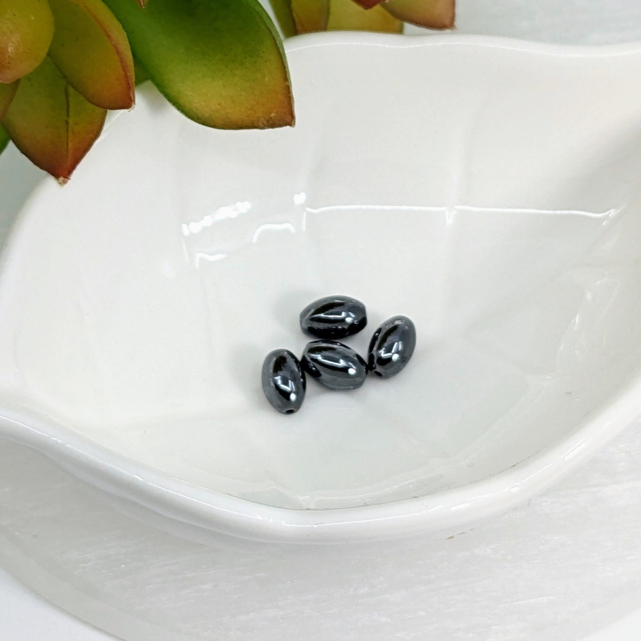 Four shiny Hematite 8mm oval beads in a pack of 4, perfect for jewelry making