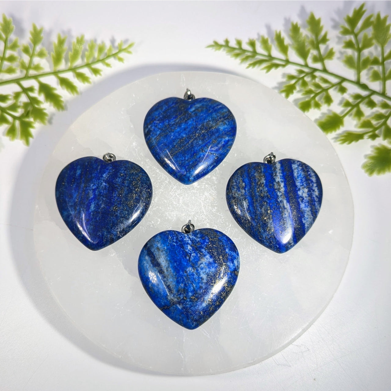 Four lapis lazuli 1.5 inch heart pendants with deep blue and silver streaks and metal loops perfect for jewelry and crystals