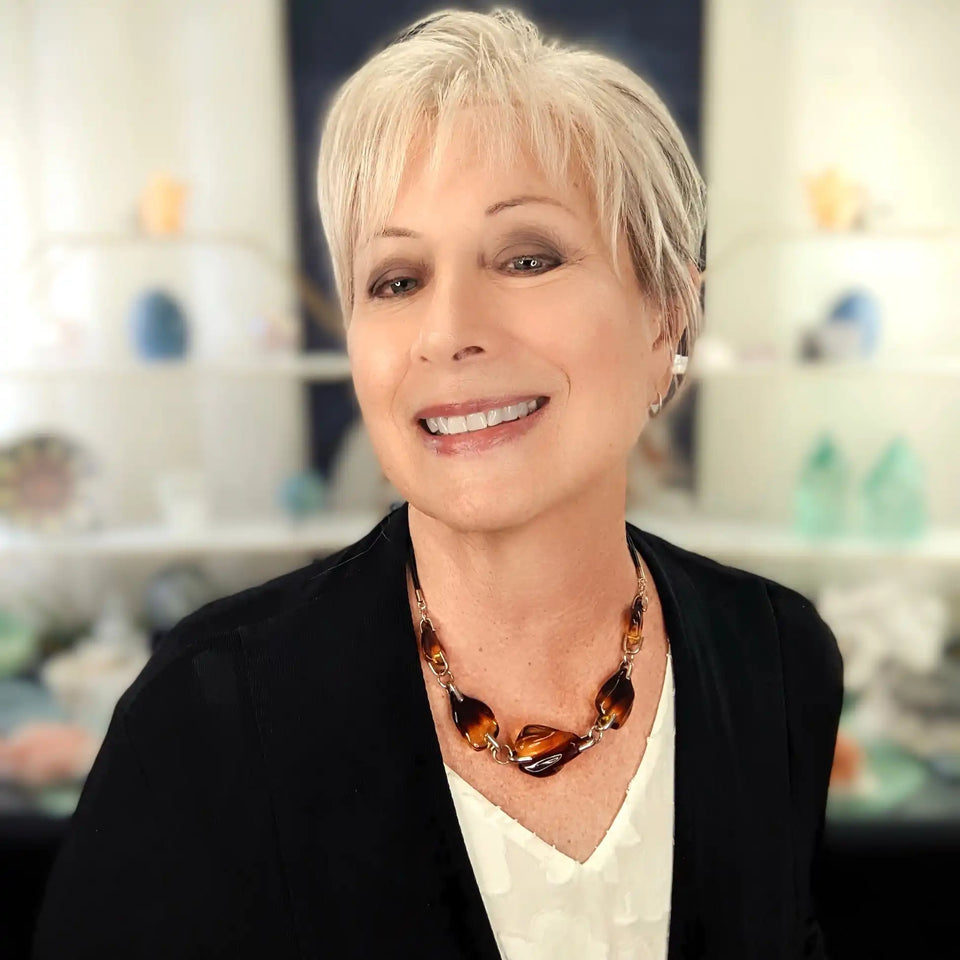 A smiling person wearing a black cardigan and amber-colored necklace.