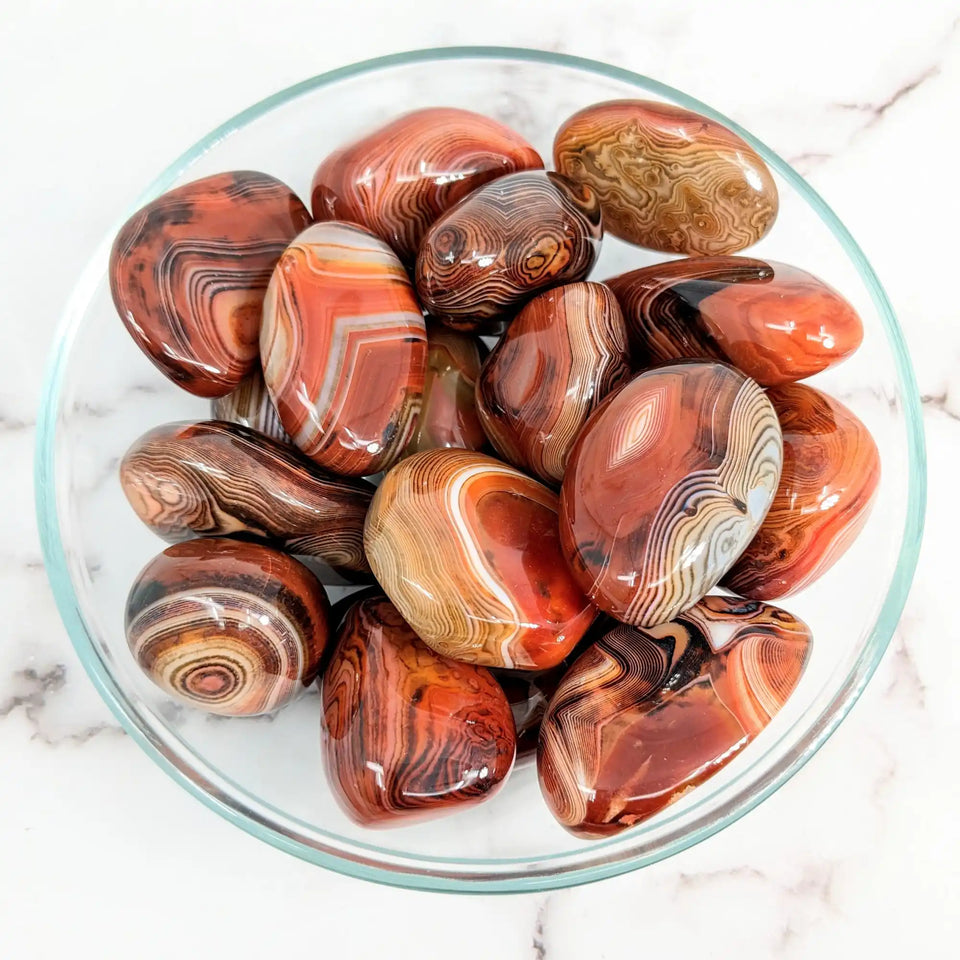 Polished red and brown banded agate stones in a glass bowl.