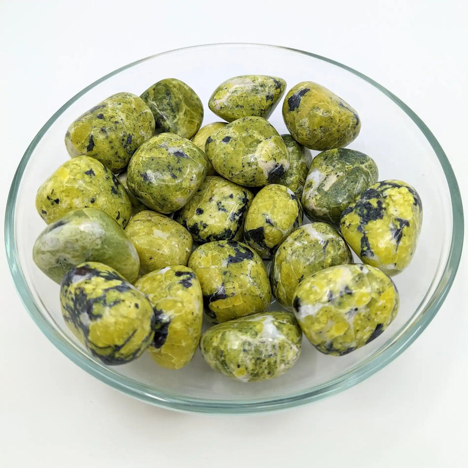 Polished yellow and black serpentine stones in a glass bowl.