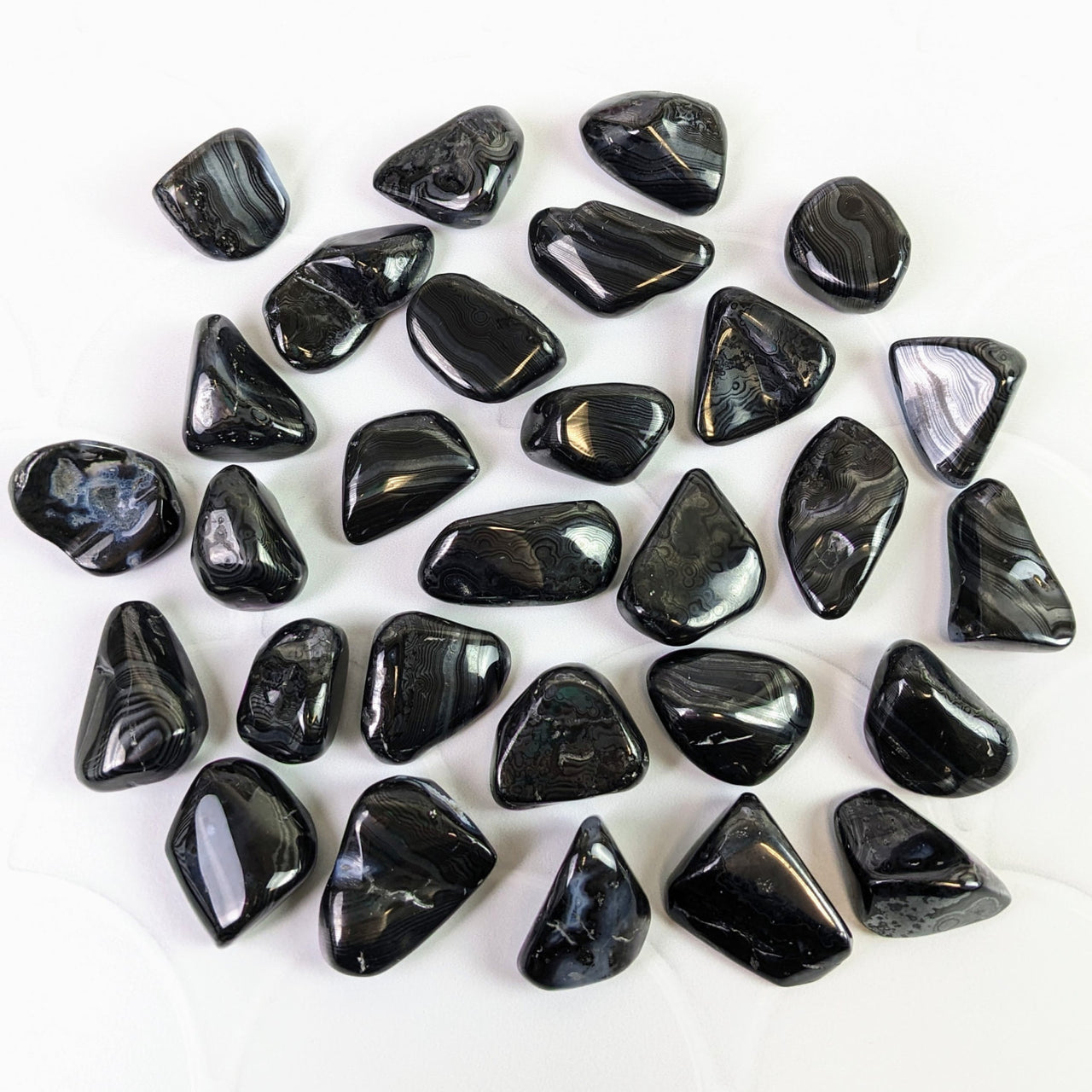 Close-up of tumbled Psilomelane black stones on white surface - Bliss Crystals #SK6310
