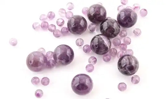Purple amethyst beads and spheres scattered on a surface.