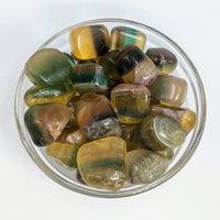 Polished yellow fluorite tumble stones in earthy colors arranged in a glass bowl