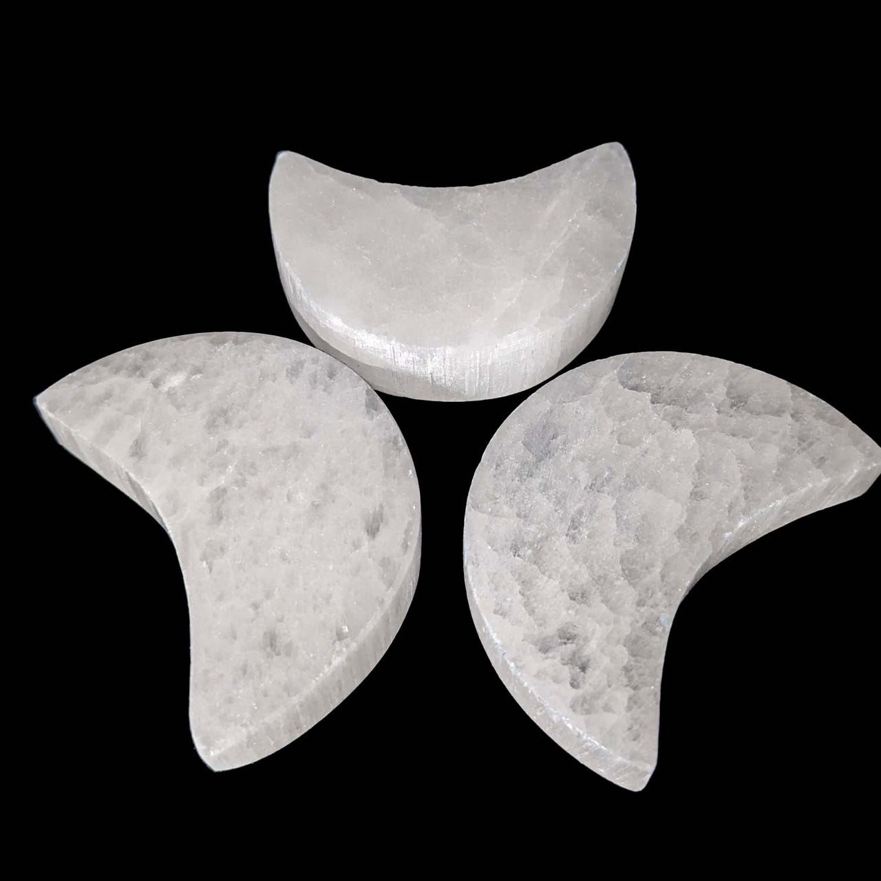 Three crescent-shaped Selenite Mini Moon Carvings arranged in a triangle