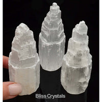 Hand holding white quartz crystal with two more beside the SELENITE Skyscraper Tower