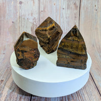 Three pieces of chocolate on a white plate beside Tiger’s Eye Rough 3’ Point #SK9983